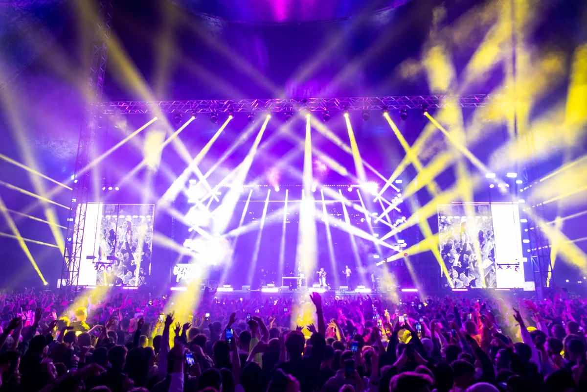 A large concert crowd at night illuminated by colorful stage lights