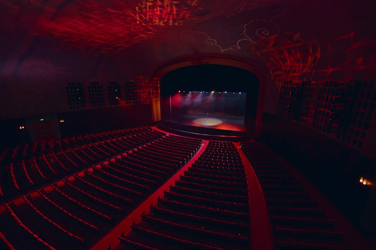 Interior of a grand theater auditorium with rows of empty red seats facing the stage