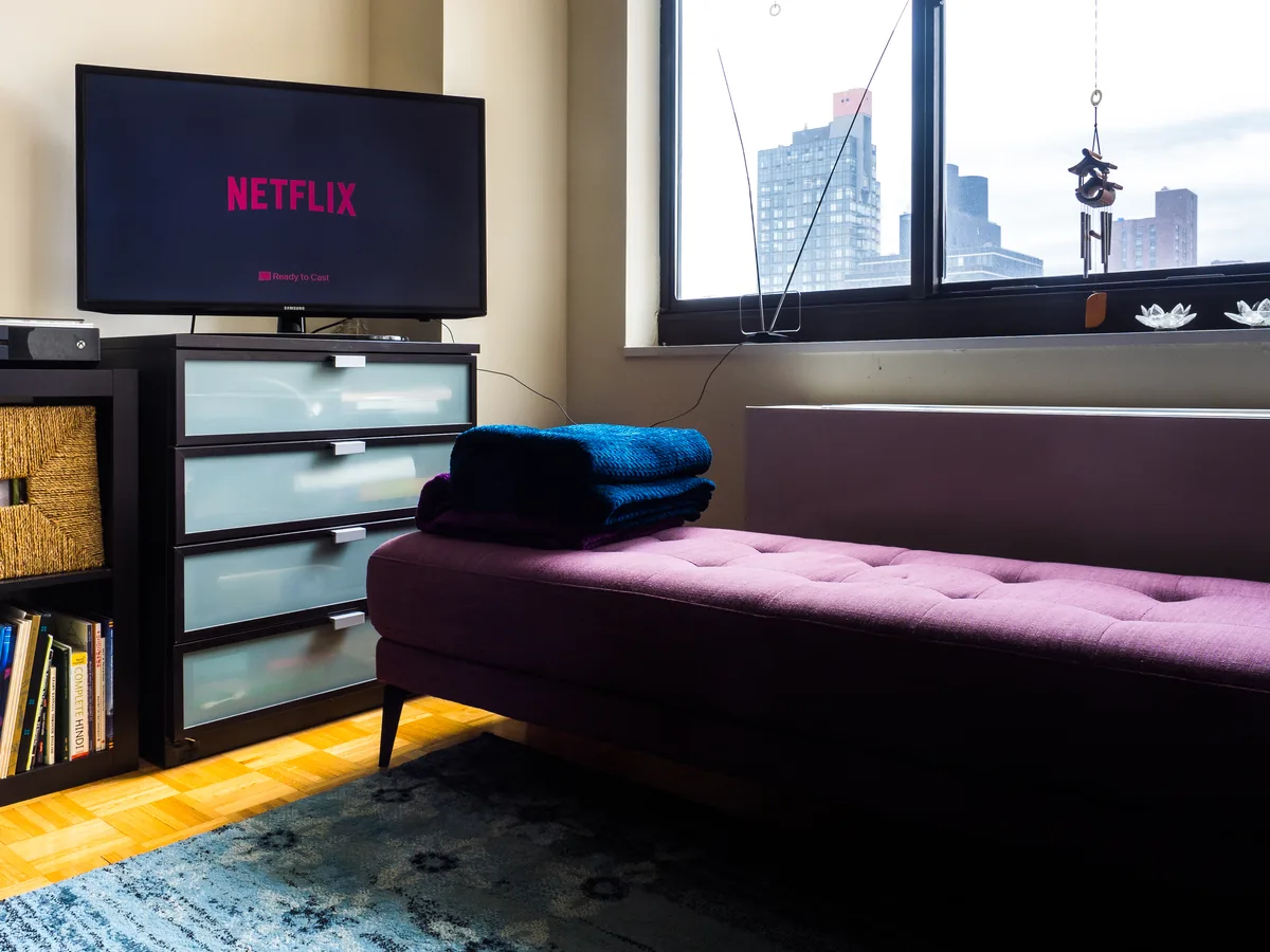 A television displaying a video streaming service interface with rows of show thumbnails